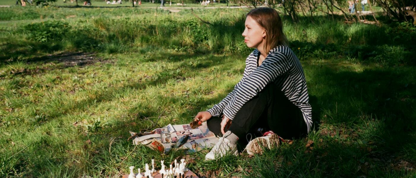 pensive woman playing chess on lawn in park