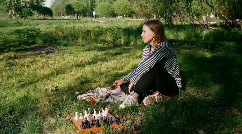 pensive woman playing chess on lawn in park
